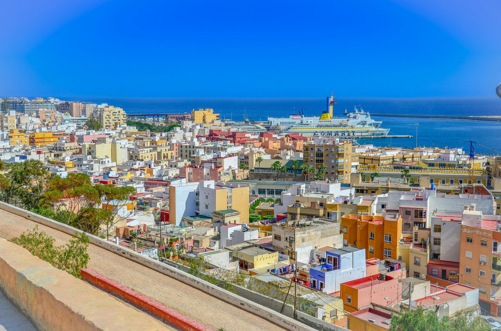 Aerial view of Almería's colorful townscape and coastline, depicting vibrant architecture and a busy harbor.